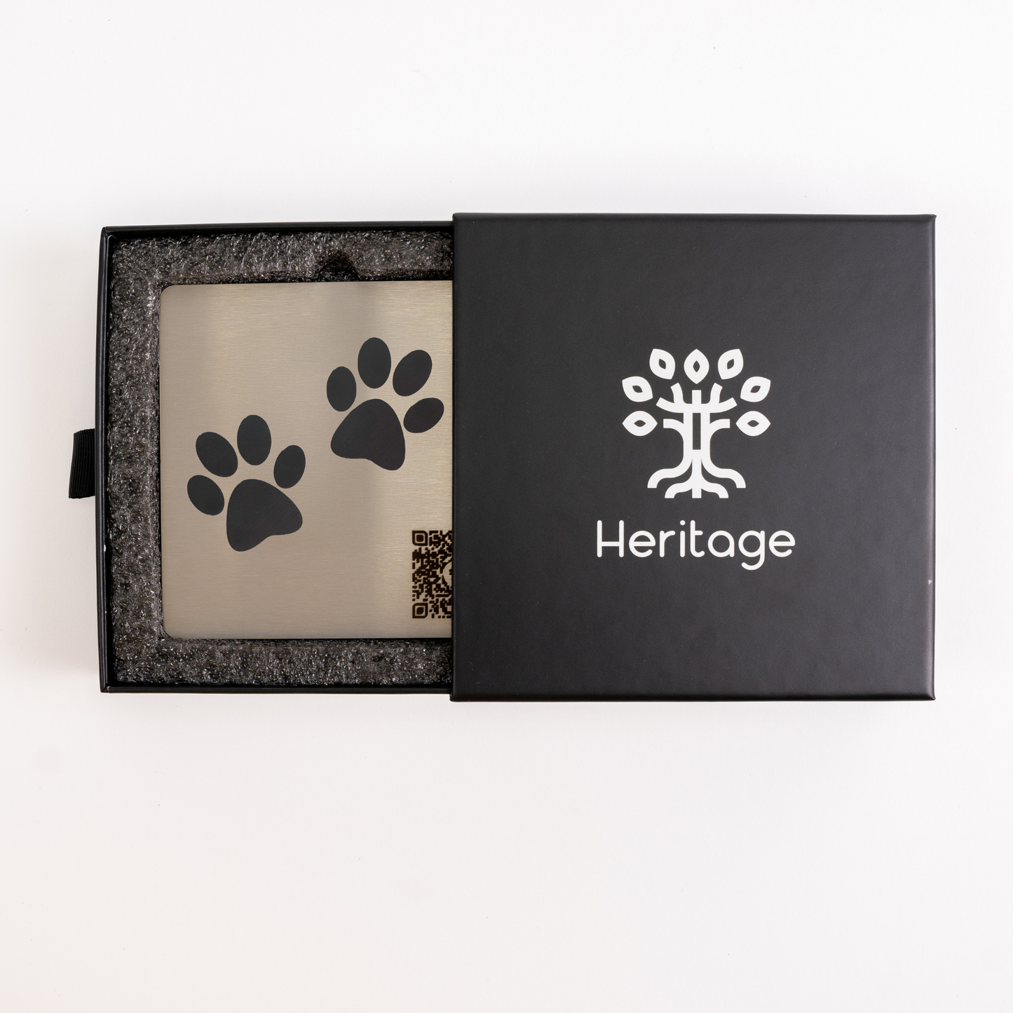 laque commémorative en acier inoxydable pour animal, présentée dans une boîte cadeau noire avec logo Heritage — gravure empreintes de pattes et code QR pour créer un profil souvenir.